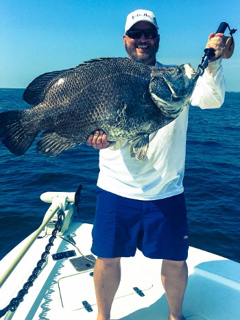 Man standing on a boat holding up a large fish.