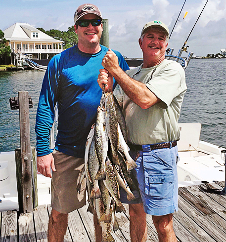 Two men standing on a dock holding a large catch of fish.
