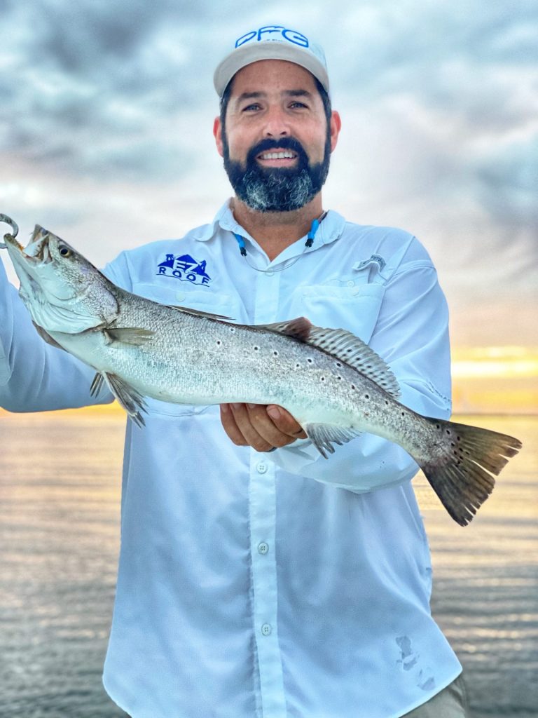 Man standing on deck holding up a large fish.